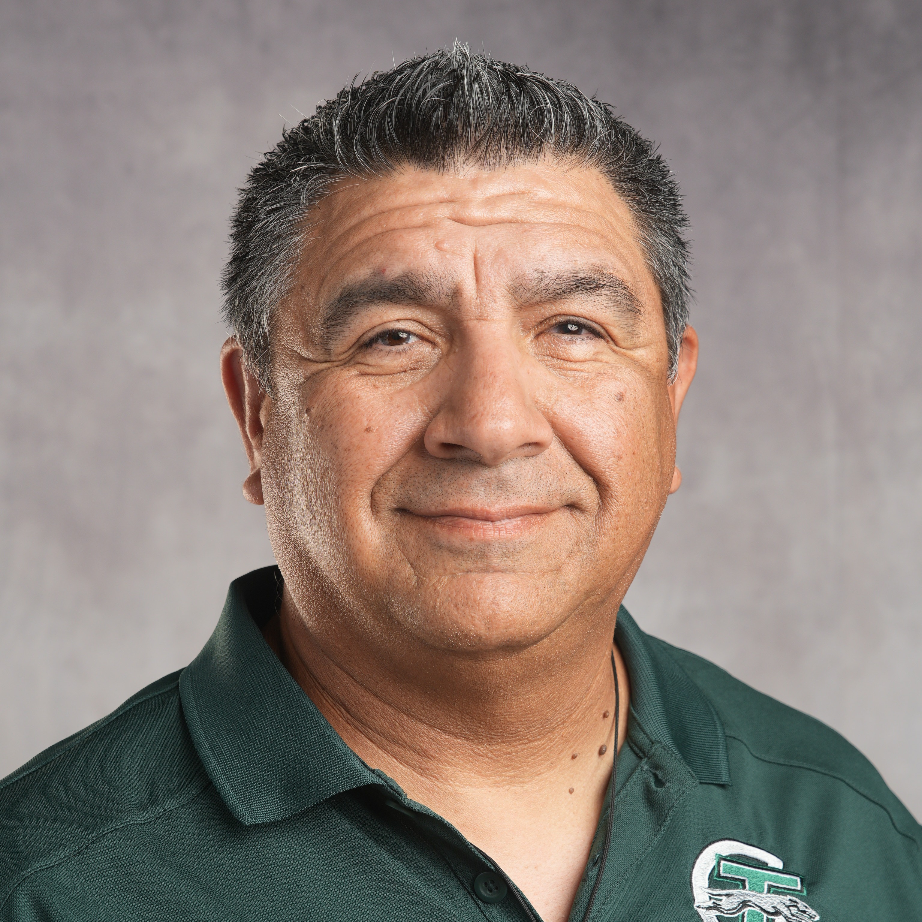 A man wearing a green polo shirt stands confidently against a solid blue background.