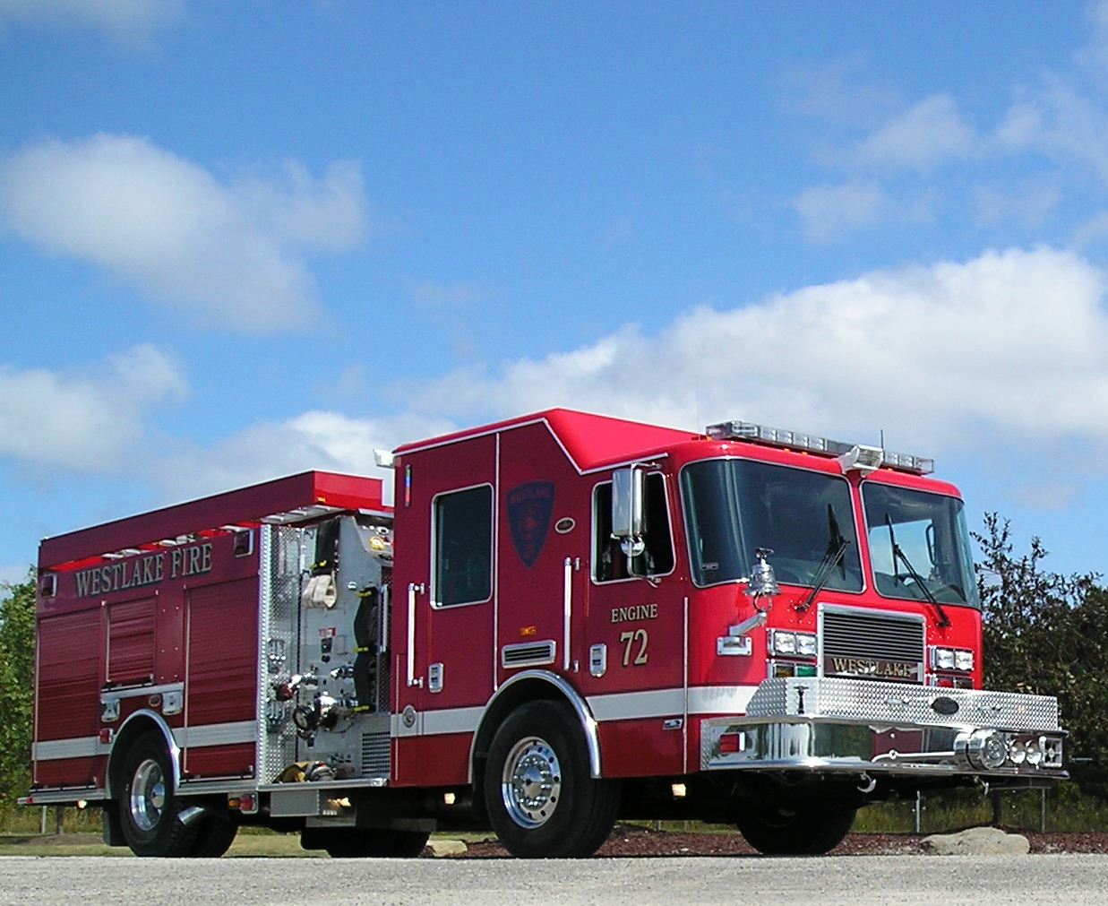 A red fire truck parked on a paved area with a blue sky and clouds in the background.