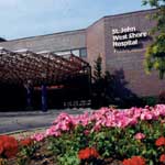 A view of St. John West Shore Hospital, featuring a landscaped area with colorful flowers in the foreground and the hospital building in the background.
