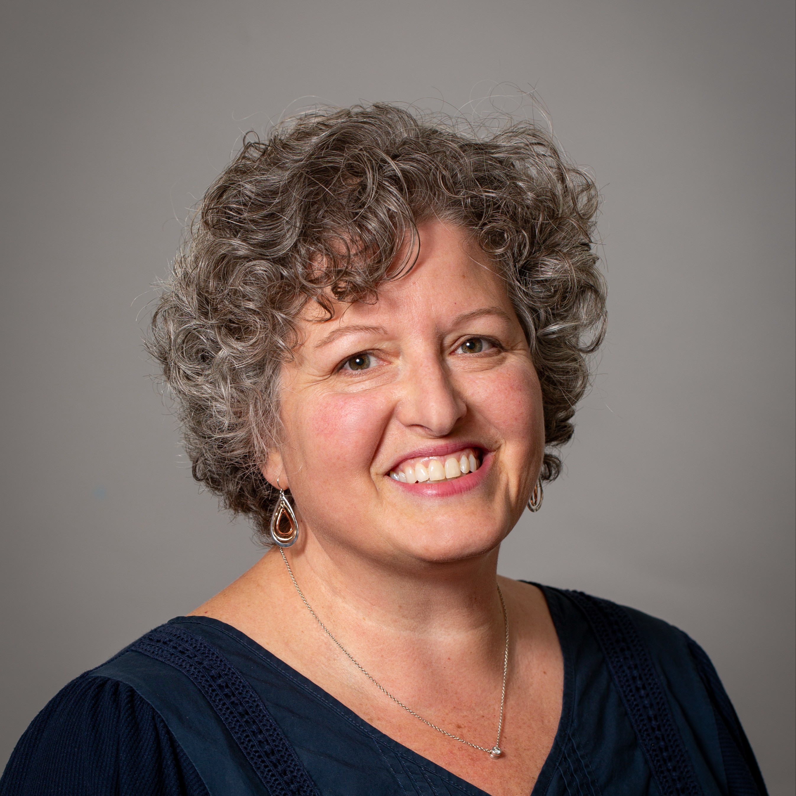 A smiling person wearing a pink baseball cap and glasses, with a light gray background.