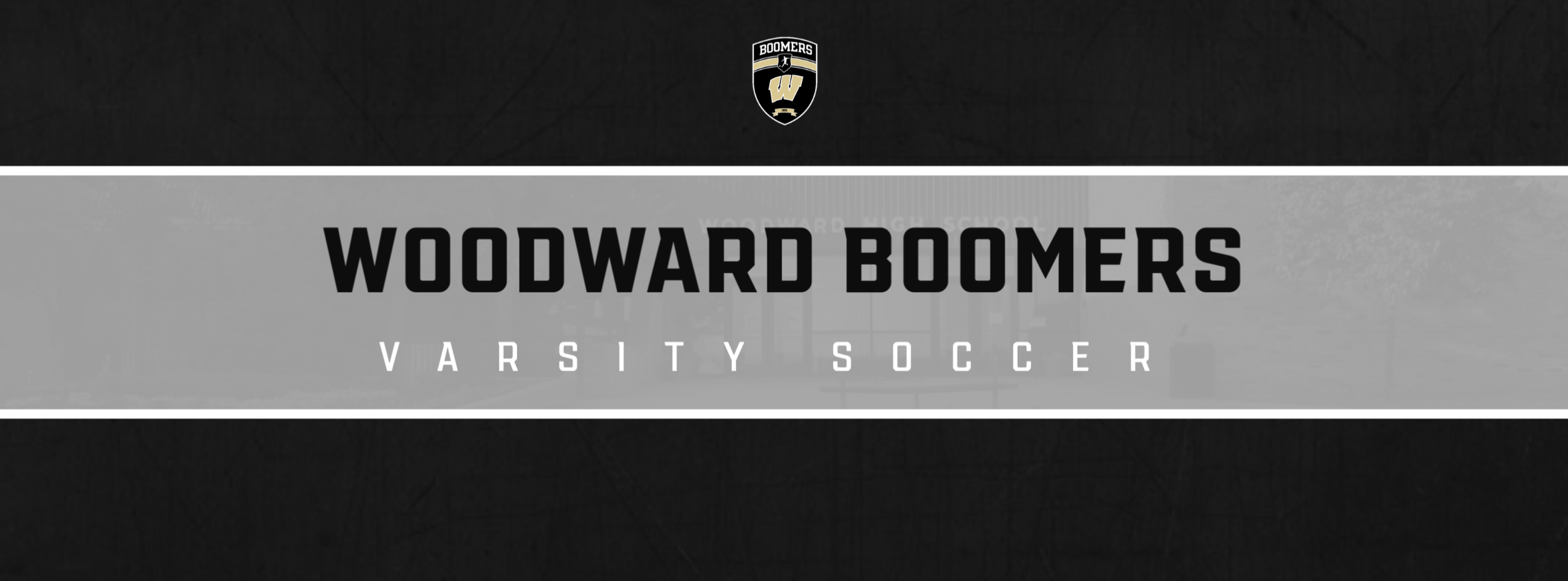 The image features a **Woodward Boomers Varsity Soccer** graphic. The background is a black-and-gray gradient with a **soccer ball** icon on the left and a faint photo of Woodward High School on the right. The **Woodward Boomers** text is bold and prominent at the center, with the word **"VARSTIY SOCCER"** underneath in a clean, modern font. The **Woodward Boomers** logo is placed at the top center of the design. The overall style is sleek and sports-focused.