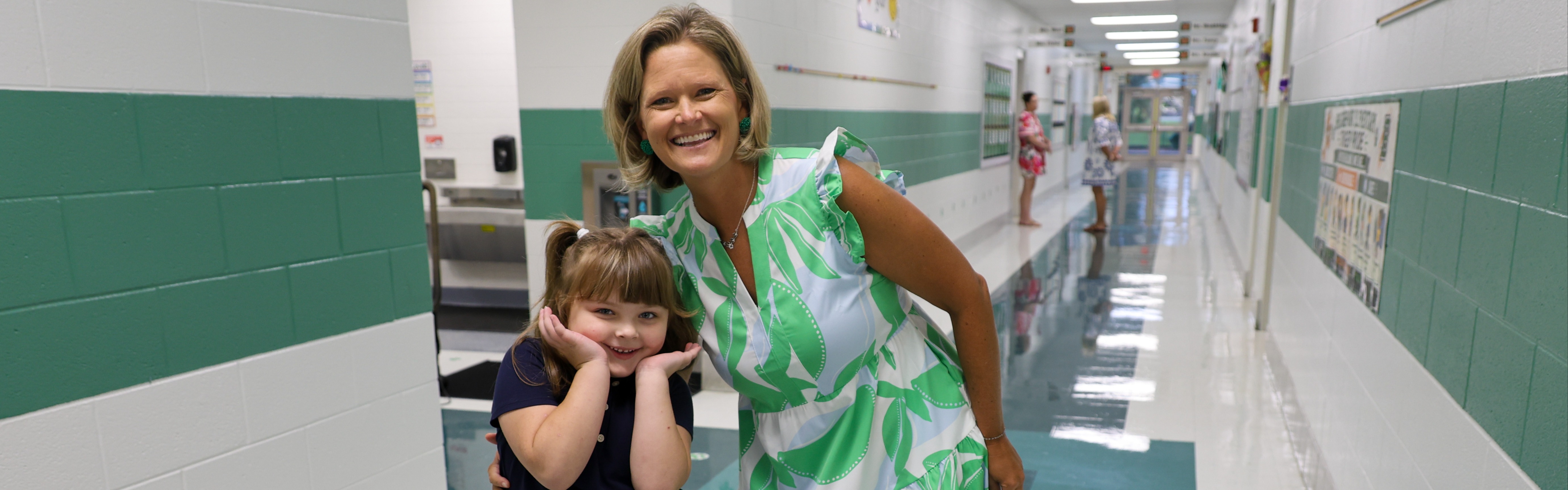 Student (left) and staff member (right) stand together in the hallway and pose for a photo.
