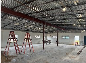 Interior view of the ROTC building renovation at Wakulla High School, showing ladders, exposed ceiling structure, lighting and ongoing construction work inside the open space.