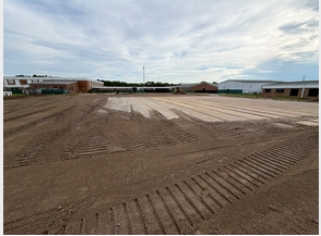 Image 4: Wide view of the Wakulla High School construction site showing a large prepared building pad with graded dirt and tire tracks as Phase 1 site work continues.