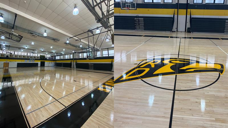 An indoor gymnasium featuring polished wooden floors, yellow accents, and a large hawk logo at center court.
