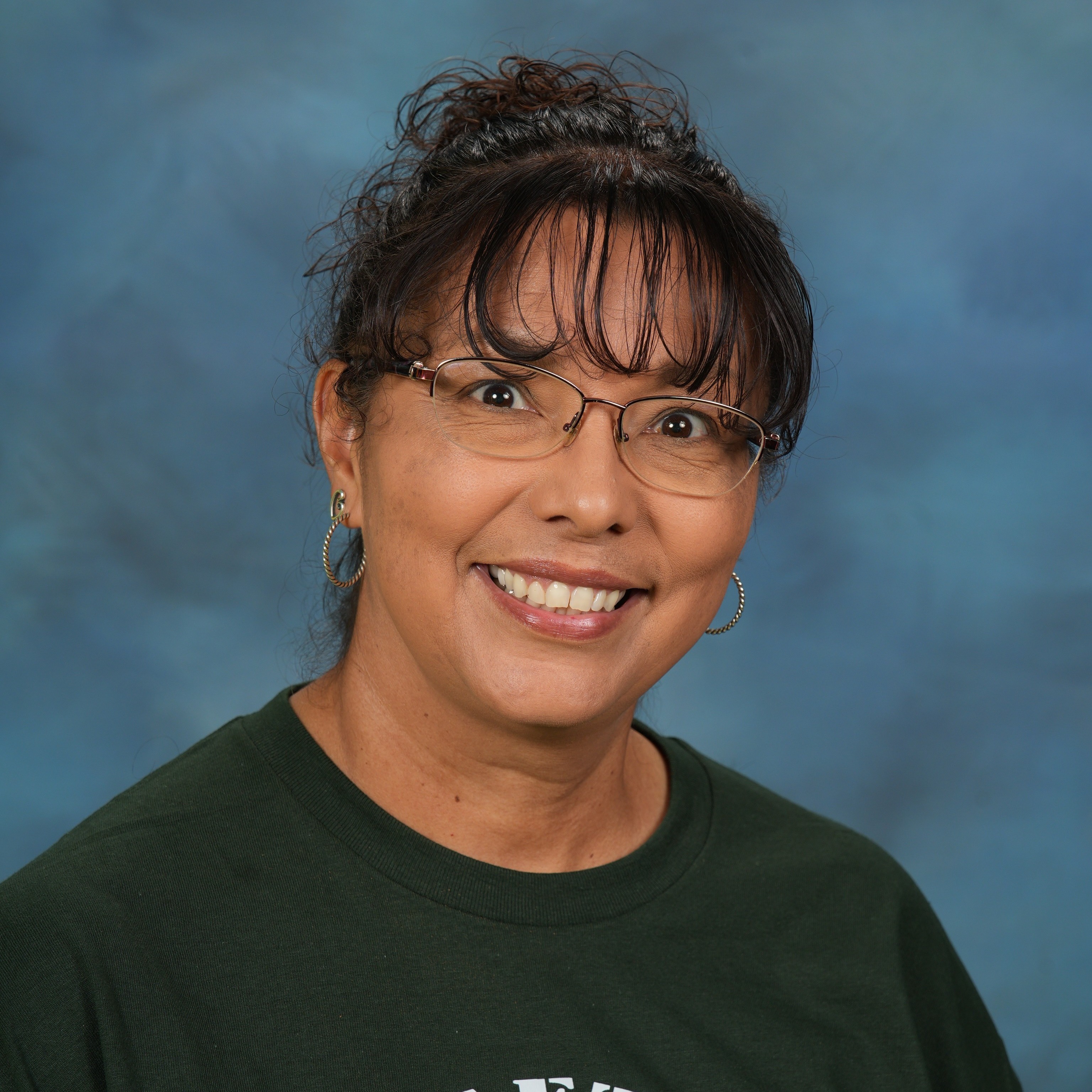 A woman wearing a green shirt stands confidently against a vibrant blue background.