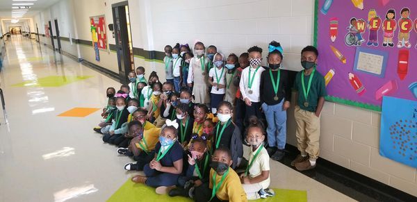 Five masked students with medals pose in front of a bulletin board, showcasing their achievements and school spirit.