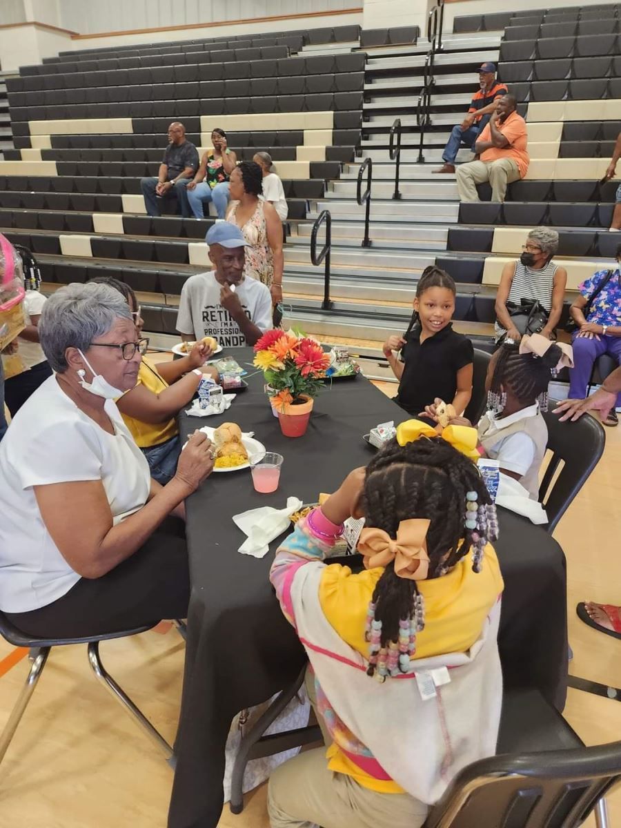 A large group of people gathered at tables in a gym, engaged in conversation and activities.