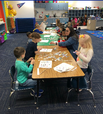 Children engaged in a classroom activity, using paper and scissors at a table, fostering creativity and collaboration.