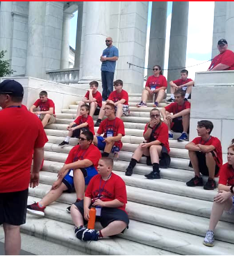 A diverse group of individuals seated on steps in front of a building, engaged in conversation and enjoying the surroundings.