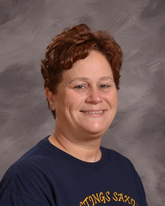 A woman wearing a blue shirt smiles warmly at the camera, exuding a cheerful and friendly demeanor.
