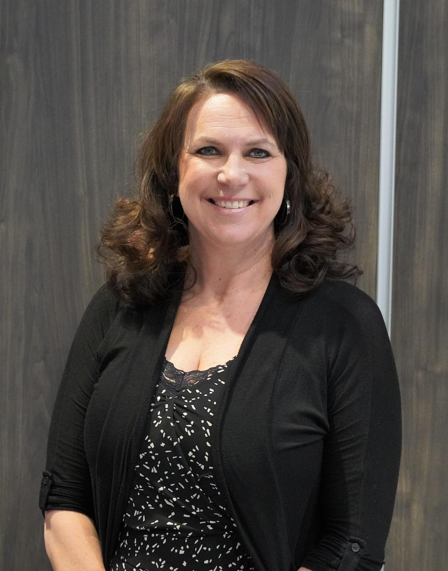 A woman wearing a black top and a black cardigan, standing confidently with a neutral expression.