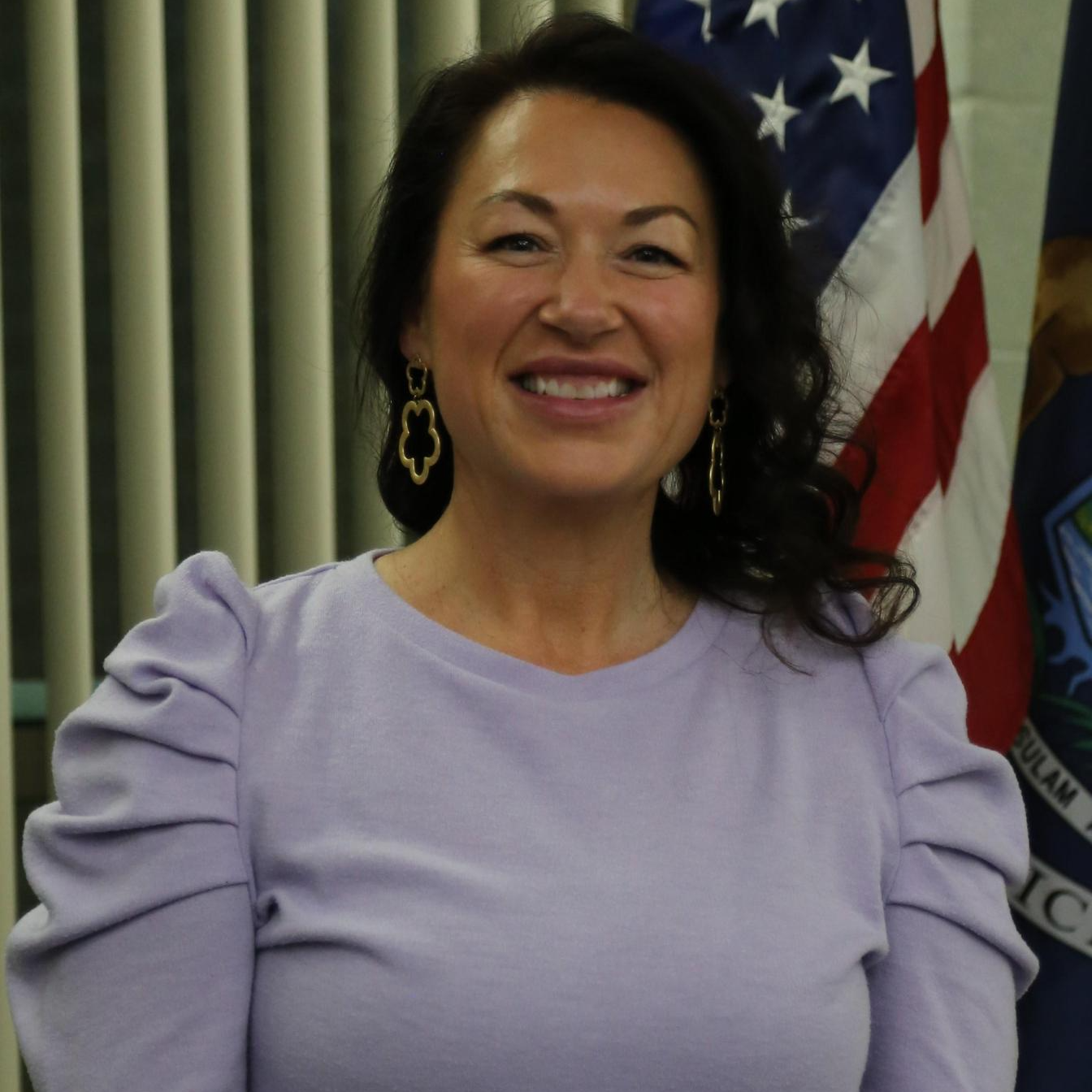 A woman in a purple shirt stands confidently in front of various flags, showcasing a vibrant and diverse backdrop.