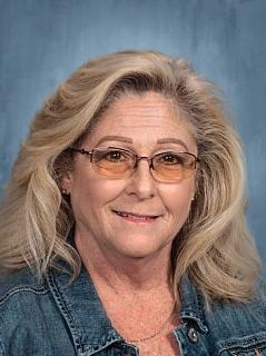 A woman wearing glasses and a denim jacket, smiling confidently against a neutral background.