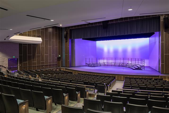 A spacious auditorium featuring rows of empty seats facing a well-lit stage, ready for an upcoming event.