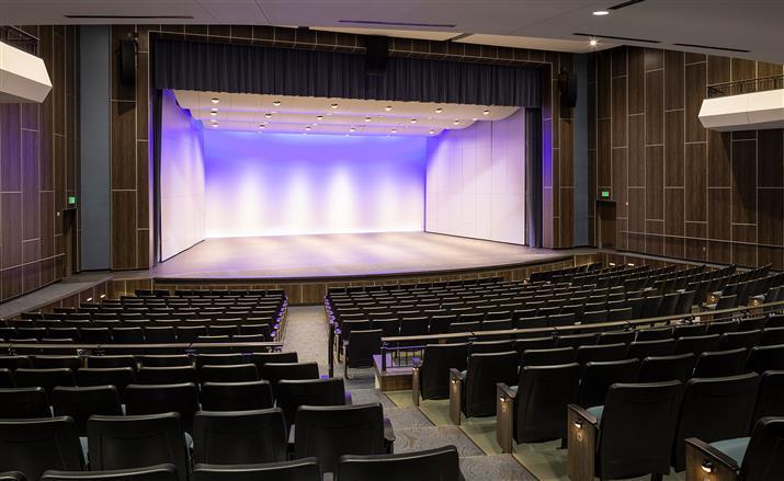 A spacious auditorium featuring rows of empty seats facing a well-lit stage, ready for an upcoming event.