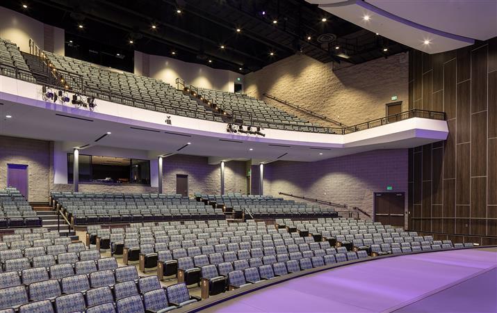 A spacious auditorium featuring rows of empty seats facing a well-lit stage, ready for an upcoming event.