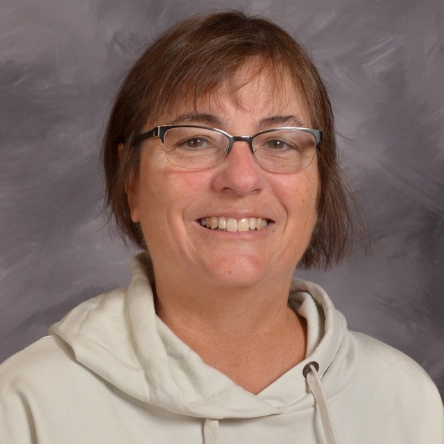 A woman wearing glasses and a blue shirt, smiling confidently in a bright setting.