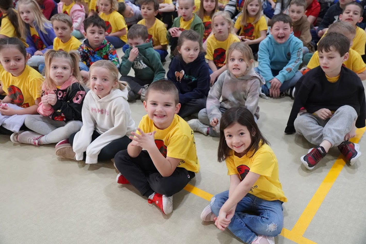 A number of children are seated on the flooring looking up at the camera with big smiles on their faces