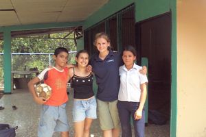 Four individuals pose in front of a building, holding a soccer ball, showcasing a moment of camaraderie and sport.