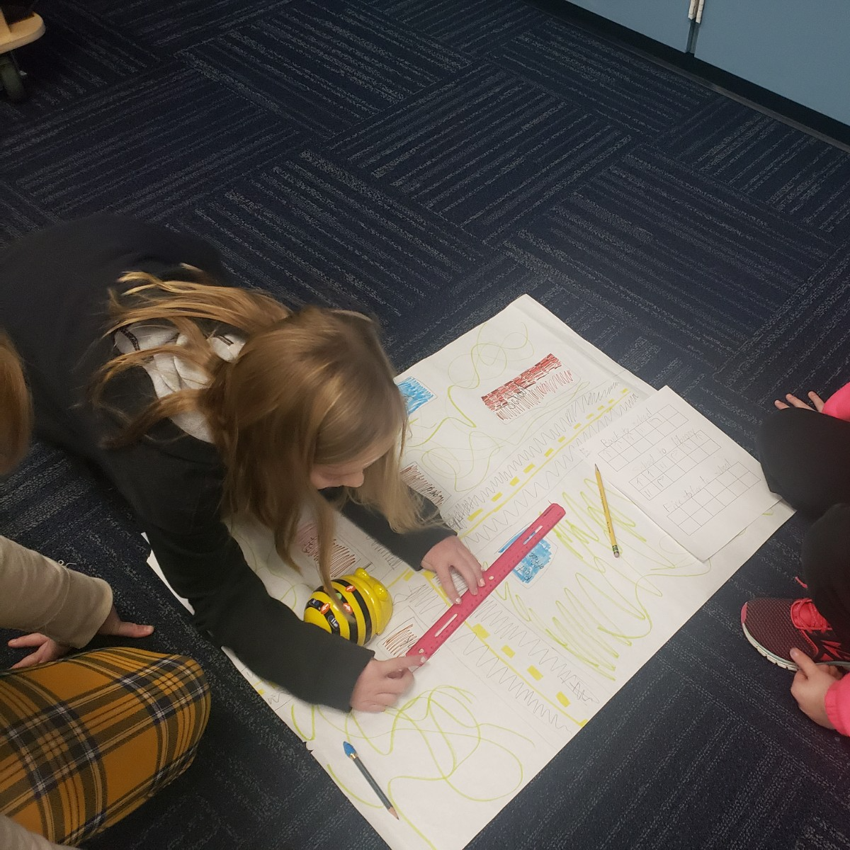 Three girls collaborate on a project while seated on the floor, surrounded by books and materials.