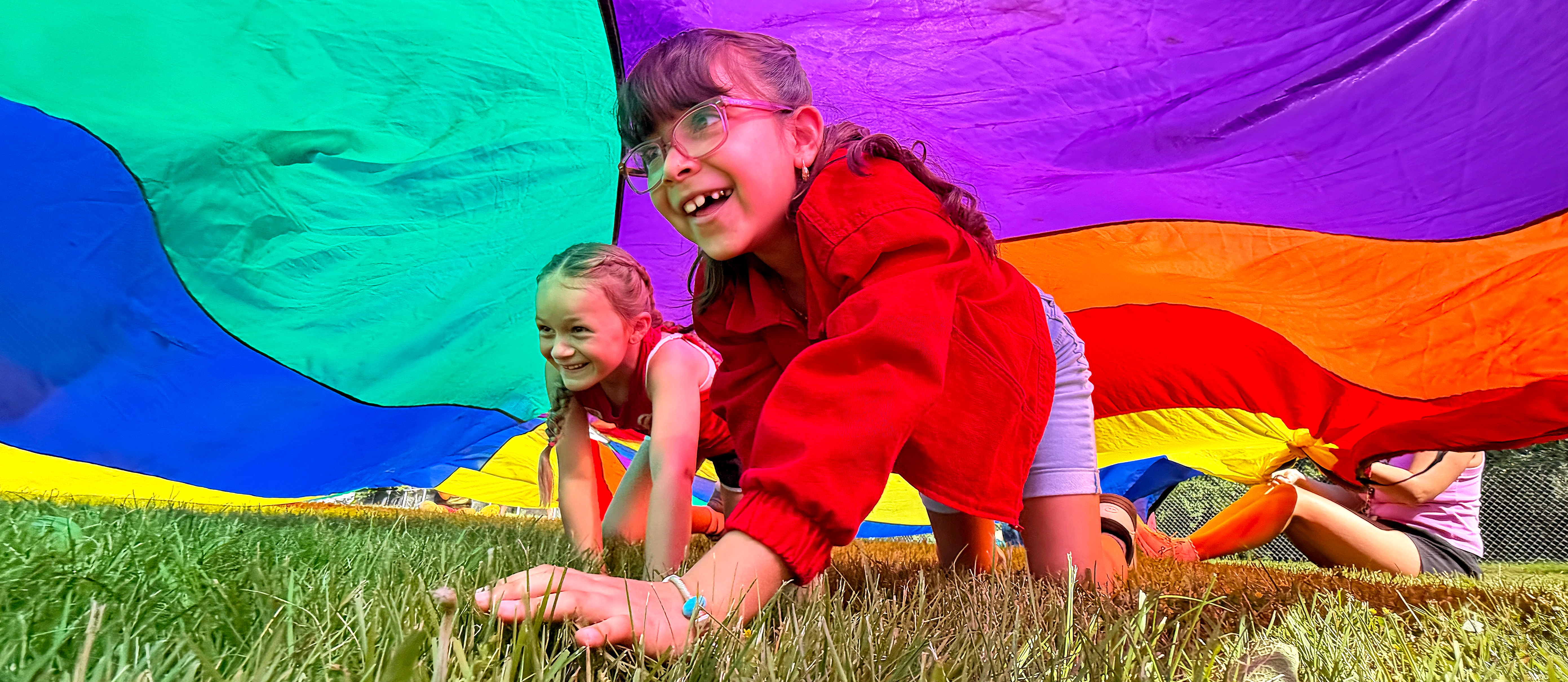 two girls crawling under a rainbow colored parachute