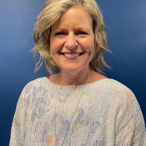 A woman in a floral blouse  with a blue wall in the background .