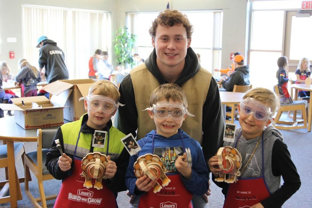Children proudly display their handcrafted turkey projects at a creative workshop, wearing festive aprons and smiling joyfully.