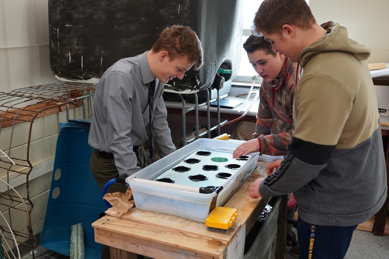 Two students work together over a tray filled with planting slots, surrounded by tools and equipment in a lab setting.