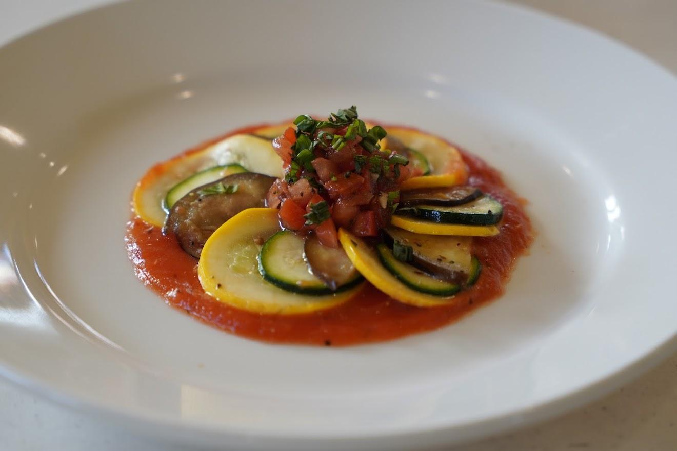 Colorful sliced zucchini and yellow squash arranged in a circle on tomato sauce, topped with fresh diced tomatoes and herbs.