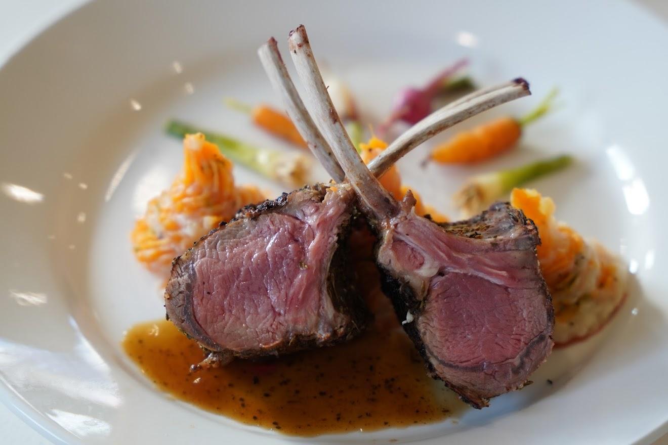 A beautifully plated dish featuring two tender lamb chops with a rich sauce, accompanied by colorful vegetables.