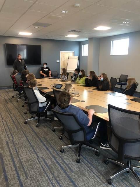 A group of students attentively listen to a speaker during a meeting in a modern conference room.