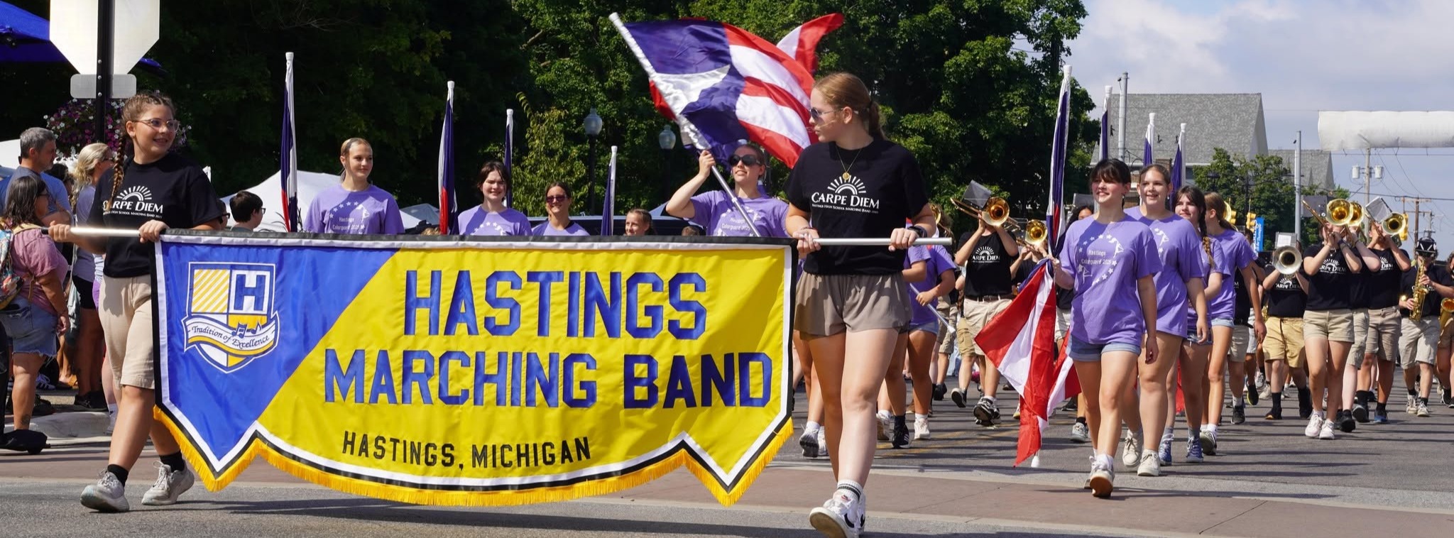A parade heads down the road led by a banner that Hastings High School