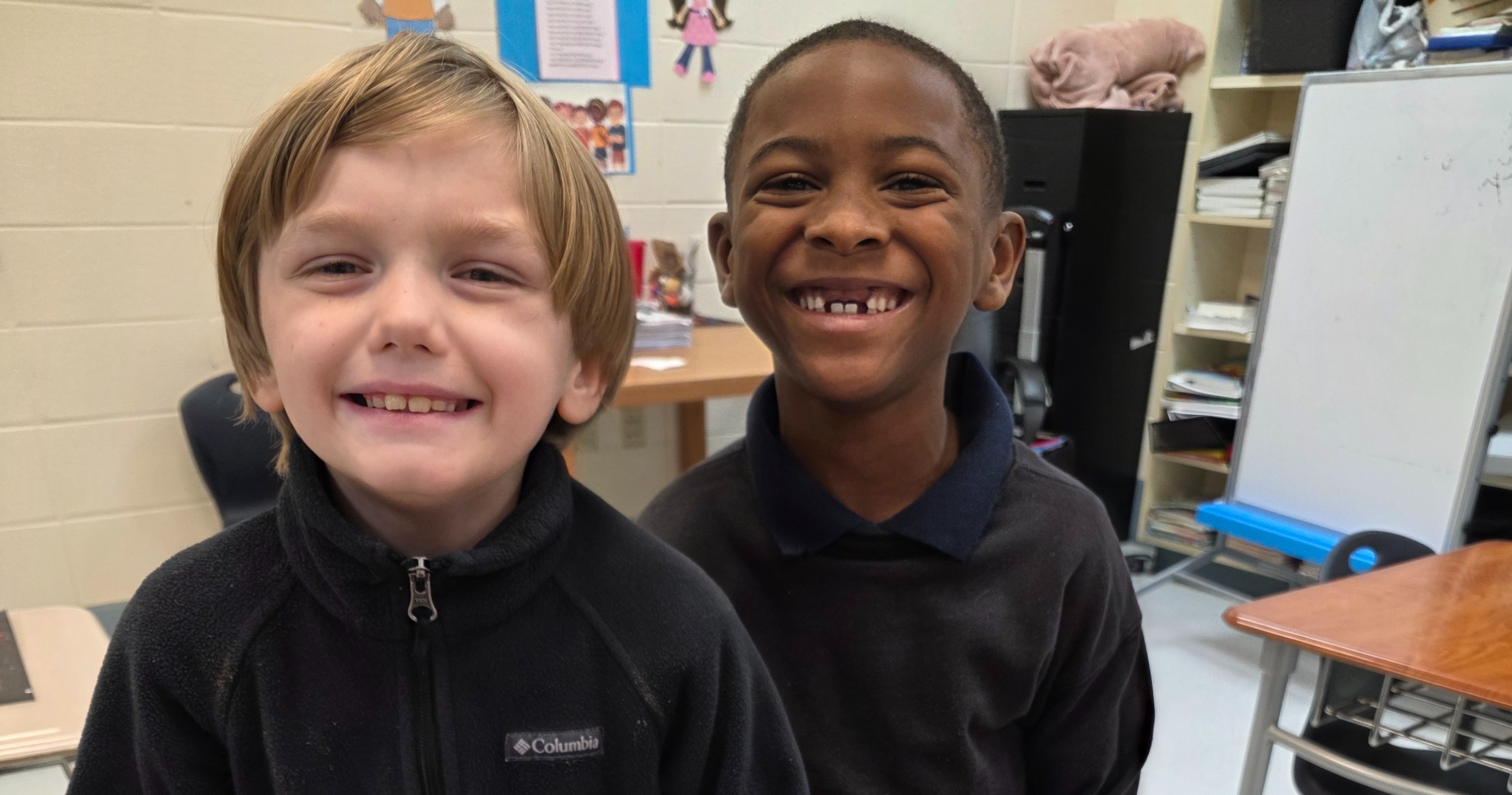 two students standing together showing off their art projects 