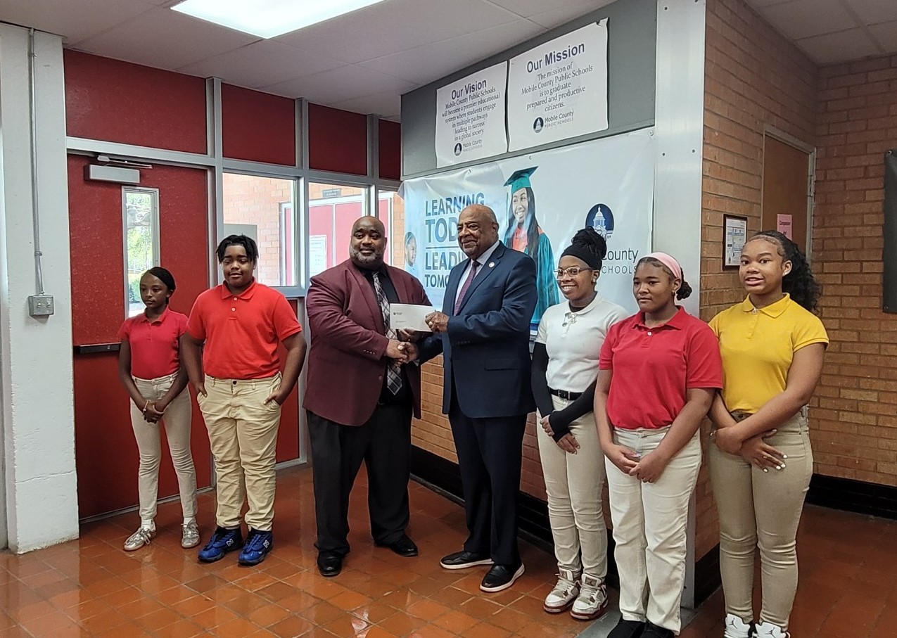 Students standing around Mr. Williams and Sam Jones while Sam Jones present Mr. Williams with a check.