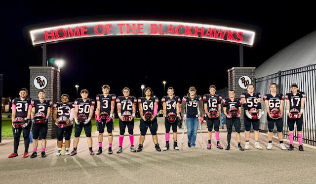 Senior football players lined up along fence on bleachers.