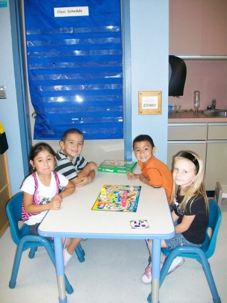 Four children engaged in a board game, sitting around a table, displaying joy and concentration in their expressions.