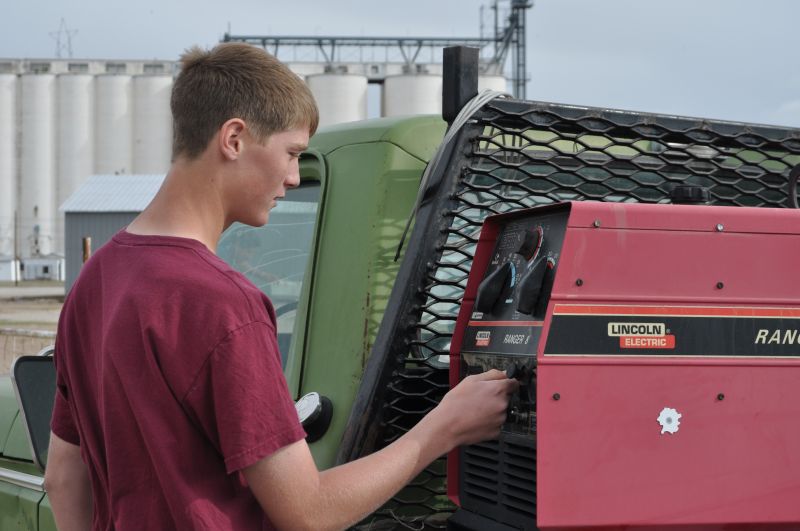 A young man operates a red tractor in a field, focused on his work under a clear blue sky.