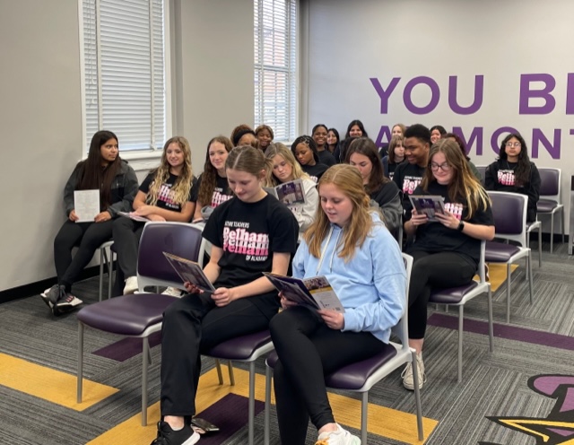Students seated in a classroom, engaged in reading books while sitting in their chairs.