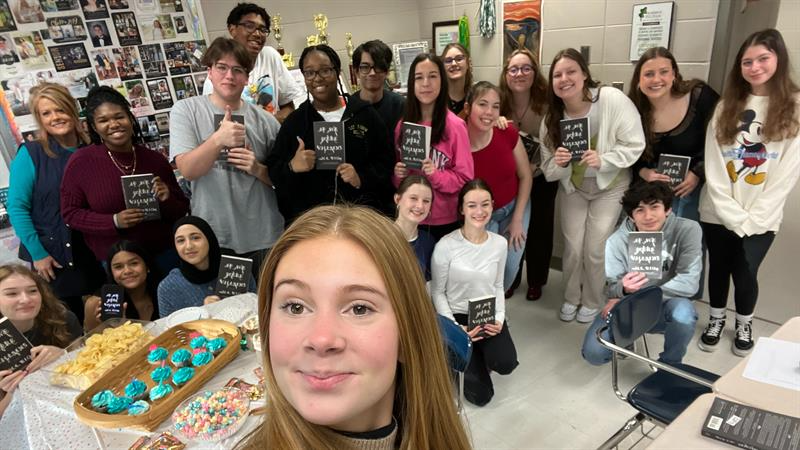 A diverse group of individuals smiling and posing together, each holding a book in a cheerful photo setting.
