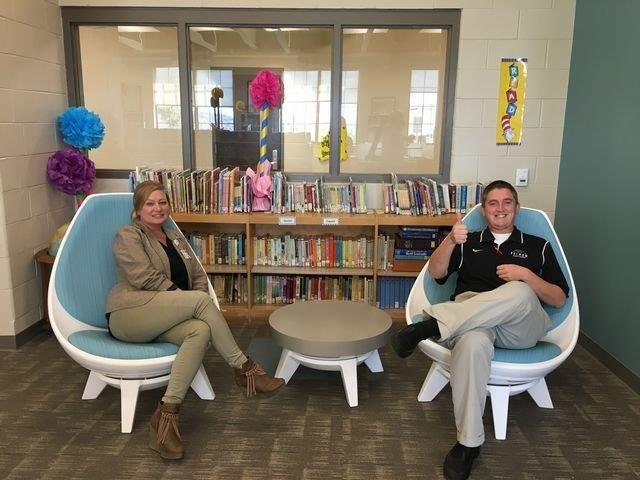 Two individuals seated in chairs, engaged in reading within a quiet library setting.