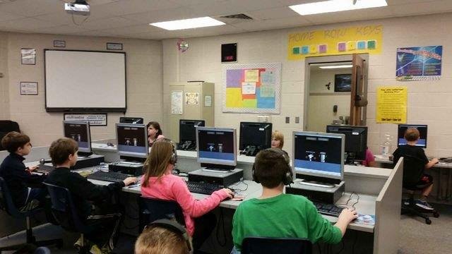 A vibrant classroom filled with children engaged in learning on their computers, showcasing collaboration and technology use.