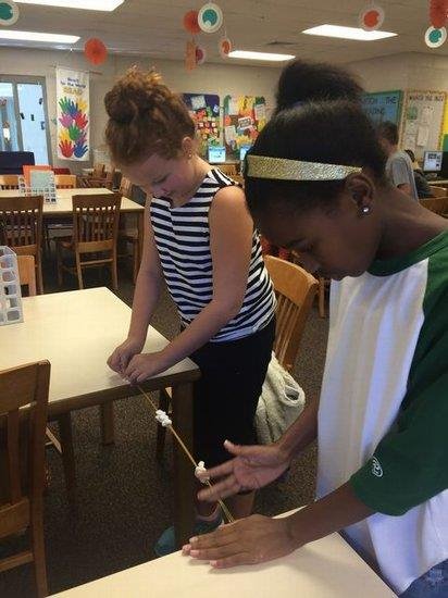 Two girls collaborate on a project together in a classroom setting, focused and engaged in their work.