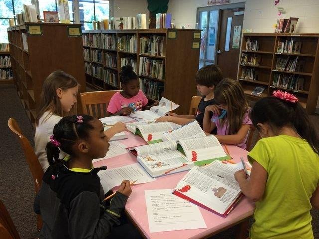 A group of students studying together in a library, surrounded by books and focused on their work.