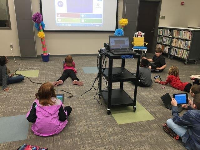 Students in a library engaged in watching a video on a laptop, surrounded by books and study materials.