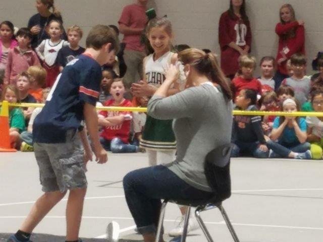 A woman sits on a chair, gently holding a child in her lap, both appearing relaxed and engaged in a moment together.