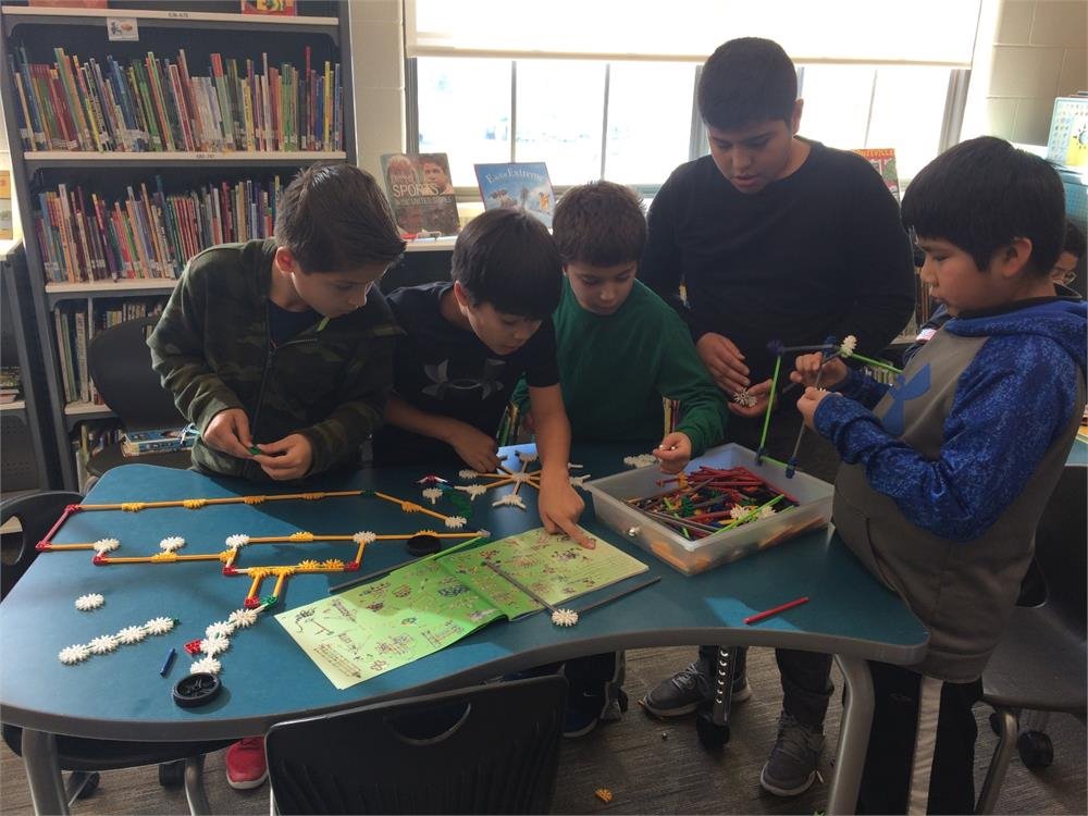 A group of children collaborating on a project together in a library setting, surrounded by books and study materials.
