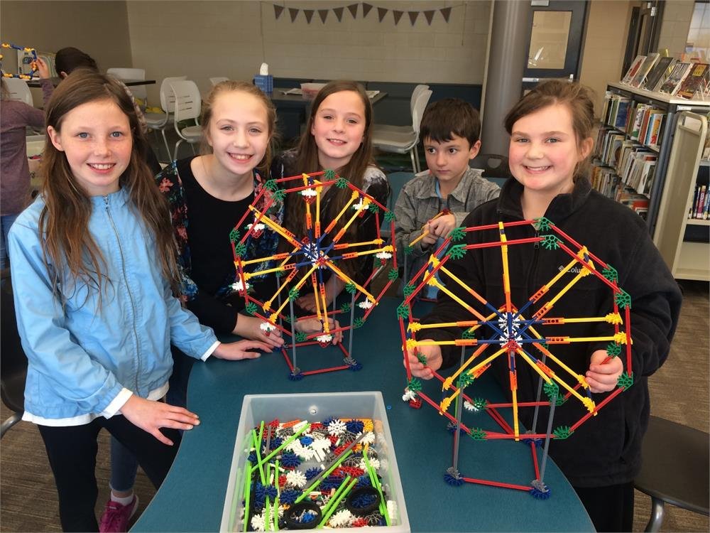 Students collaborating in a library, constructing a model ferris wheel with various materials and tools.