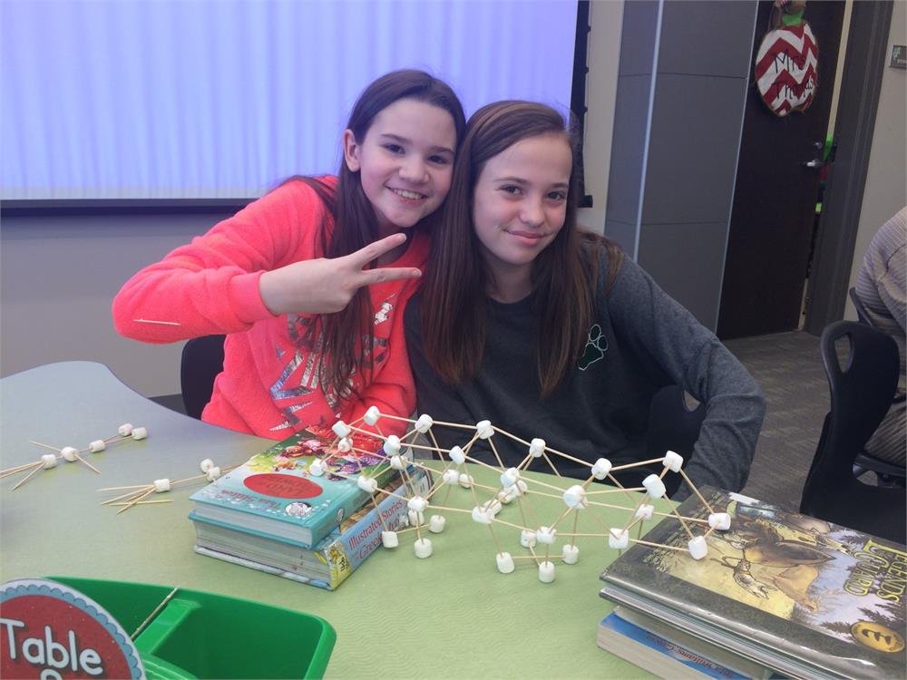 Two girls smile for a photo at a table surrounded by books, showcasing a moment of friendship and learning.