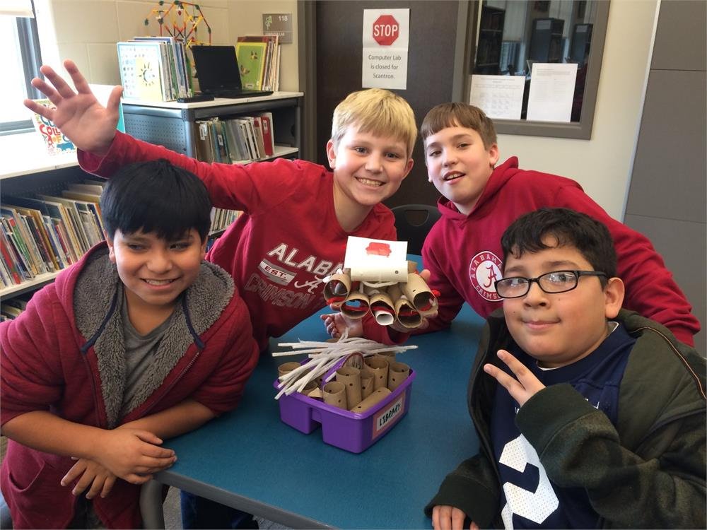 Three boys smile for a photo in front of a table displaying an open book.